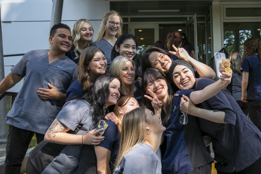 A group of students in medical scrubs pose for selfies. 