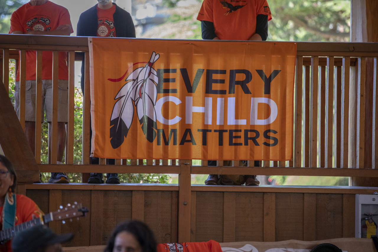An orange banner that says Every Child Matters hangs from a railing with three people behind it.