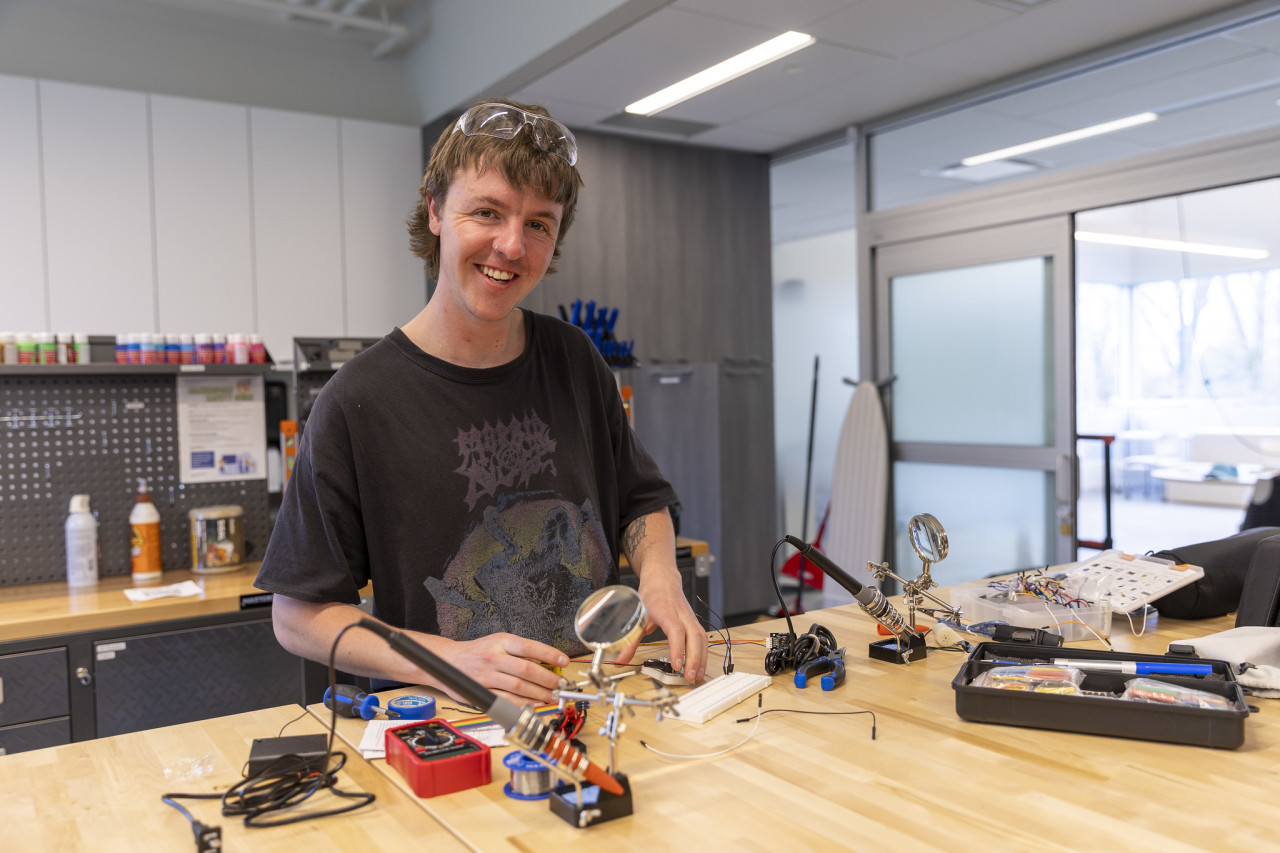 A young man happily working on a circuit board project, smiling as he focuses on assembling the parts.