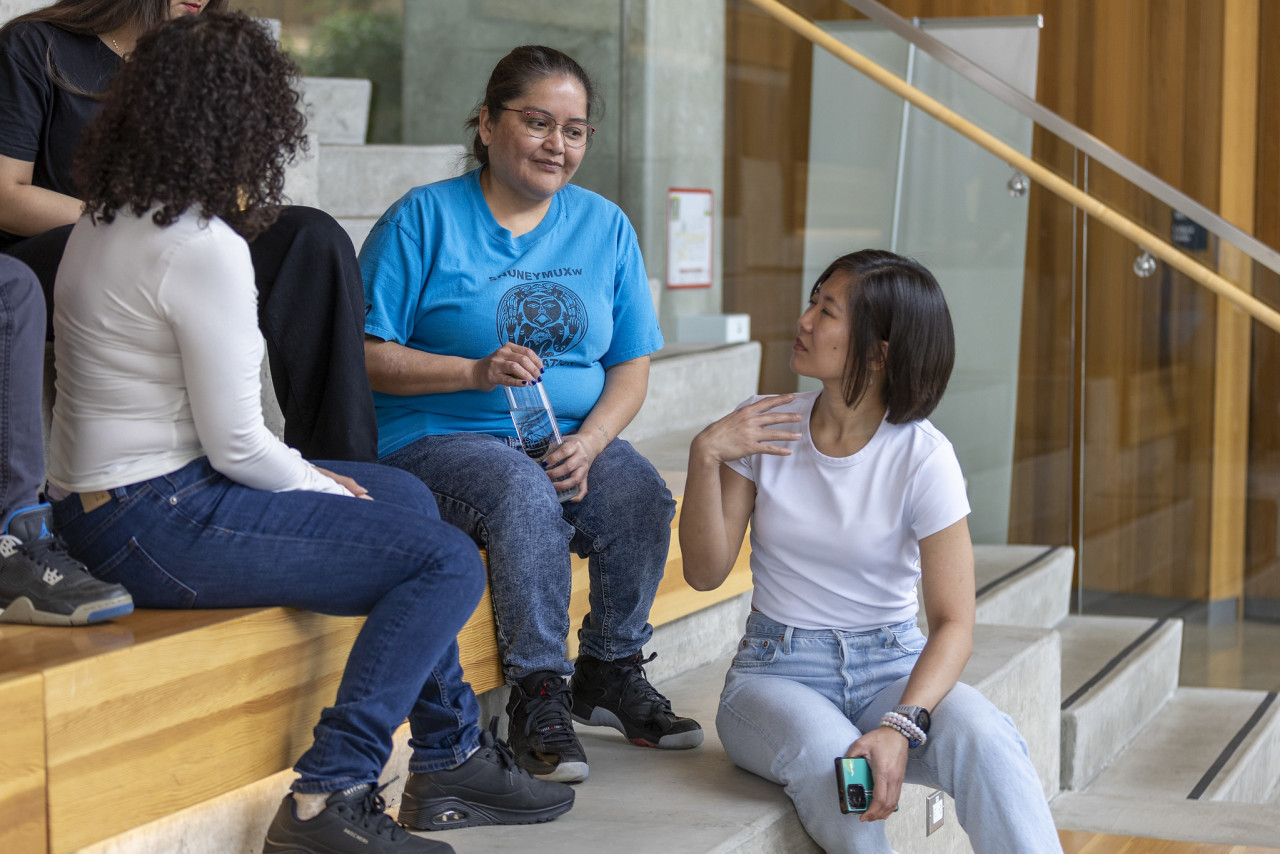 A diverse group of students sitting on steps outside a building, chatting and studying together.