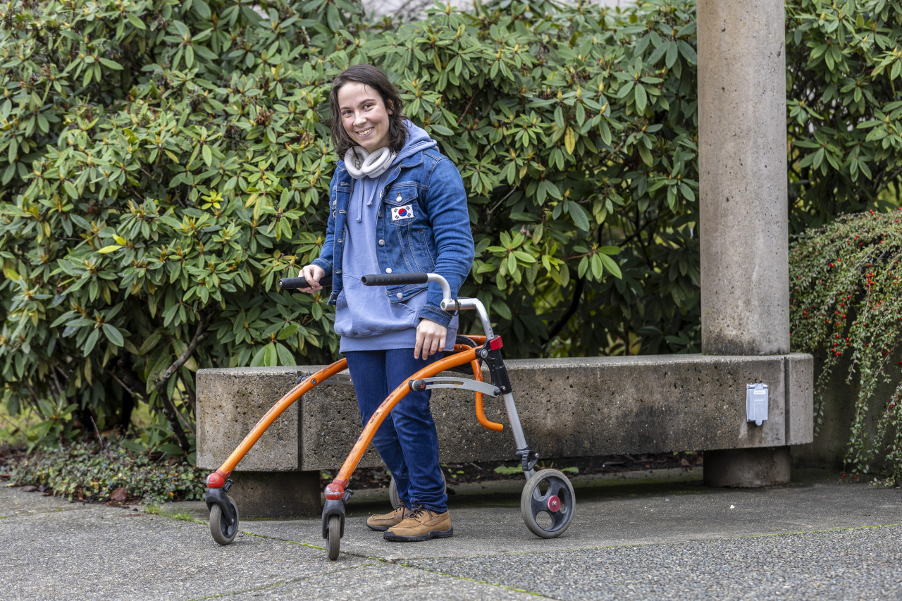 ETP student Tasha Shaw poses for a photo outdoor. Green shrubbery is in the background. Tasha is holding onto her orange walker.