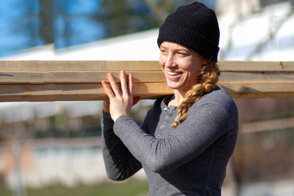 A female construction carpenter carries a load of 2x4's across a building site. 