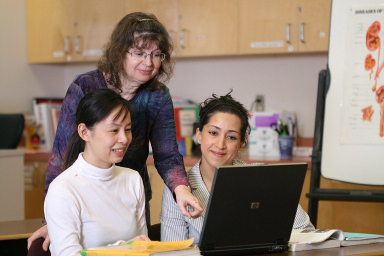 an instructor looks over a students shoulder giving feedback on an assignment