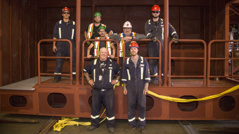 A Group of seven plumbing students on the job site wearing hard hats and coveralls.