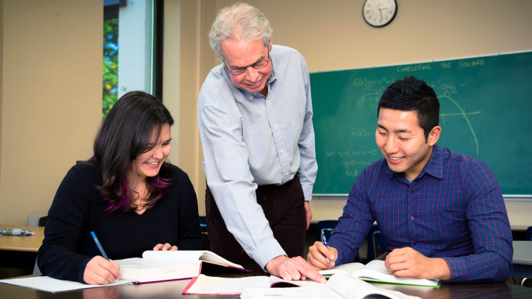 A diverse team of three individuals, consisting of a college instructor, one student in her early 20's and students and a mature student collaborating reviewing a math problem..