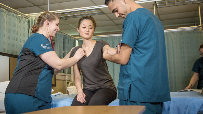 Practical nursing students practicing checking a patients heart rate 