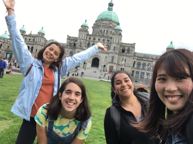A group of friends take selfies with the BC parliament buildings in the background.