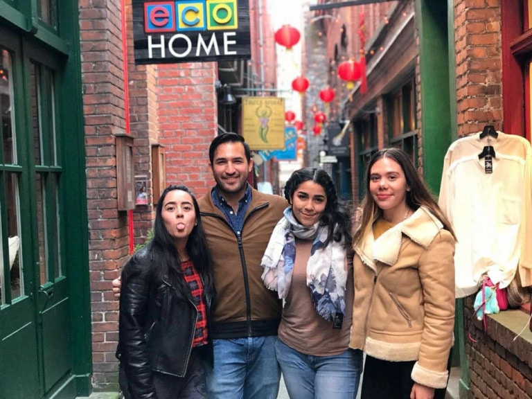 Four Camosun International students pose for a photo in a quaint, cobble stone alleyway under a sign that says 'home'.