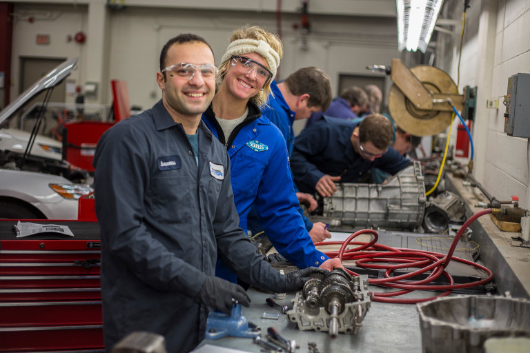 Automotive students practicing their trade at a work bench in a large automotive shop.