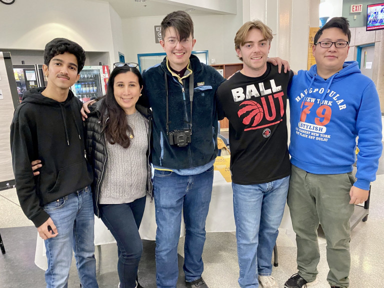 Four men and one woman stand with their arms around each other and smiles on their faces