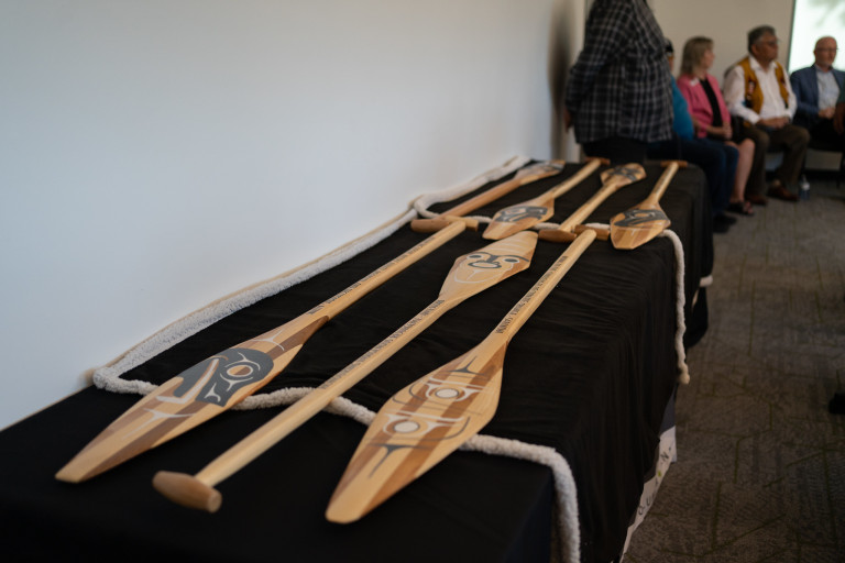 Six paddles with Indigenous artwork lay on a table with a black background