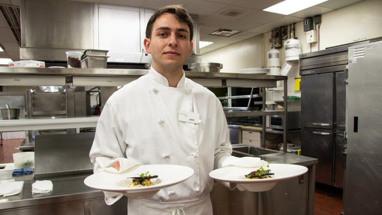 A chef holds out two beautifully plated meals for a fine dining experience.