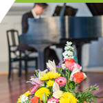 Pianist in distance playing piano during awards ceremony with bouquet of yellow and pink flowers in forefront