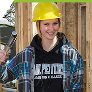 A woman in a hard hat working on framing a house. 