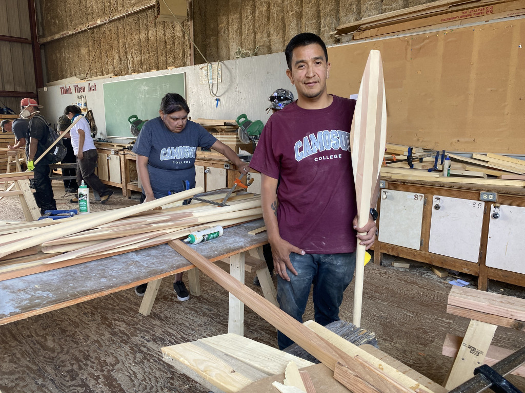 A man stands with a canoe paddle in a woodworking shop