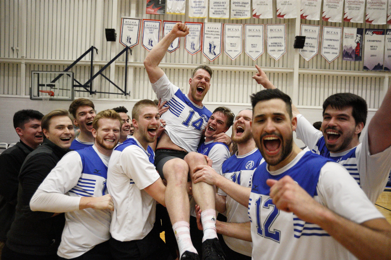 Teammates hoist a volleyball [player onto their shoulders celebrating a win