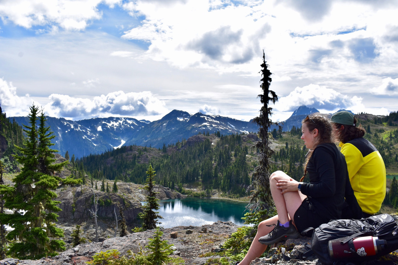 two adventure education students sitting on rock ledge overlooking mountain forest and lake view in Strathcona Park 