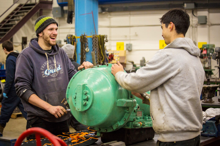 Automotive Service Technician Foundations students smile as they work on an genine