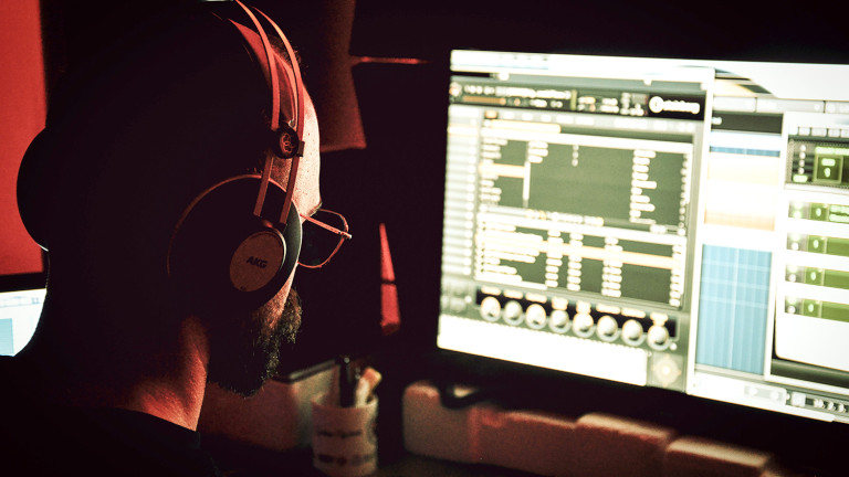 A man with headphones sits editing music at a computer.