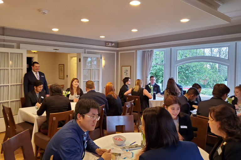 Students seated at large tables network and interact in a dining room