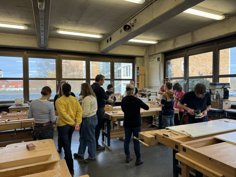 A group of carpentry students gather in a wood working shop